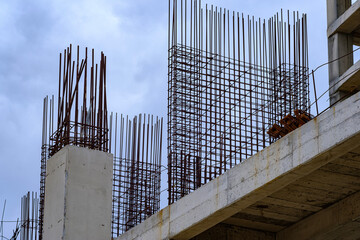 Steel reinforcement bars or rebar sticking out from concrete columns at a building construction site against a cloudy sky
