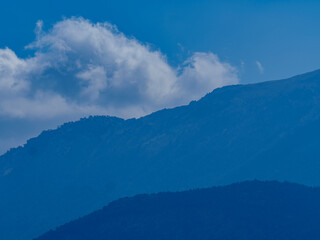 Obraz premium A dramatic view of a dark blue mountain peak with a soft white cloud touching its summit against a clear blue sky a majestic nature landscape