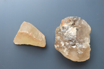 Close-up of rough chunk of translucent smoky quartz or raw mineral isolated on a dark surface. Represents geology, earth science, raw material, abstract texture, and gem concept.