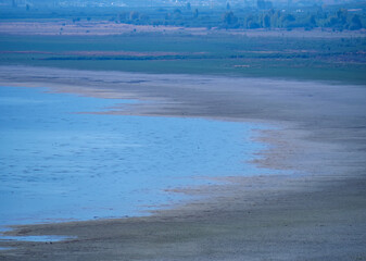 A wide and serene landscape of a shallow lake or wetland with patches of water and marshland under a hazy sky