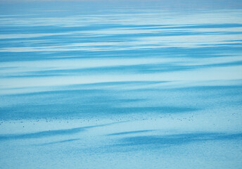 An abstract texture of a calm blue lake surface with beautiful light and shadow patterns creating a serene and mesmerizing background