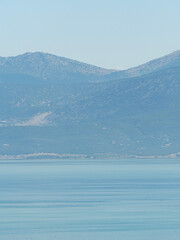 A minimalist vertical photograph of a hazy mountain peak rising above a calm and serene blue lake creating a peaceful nature scene