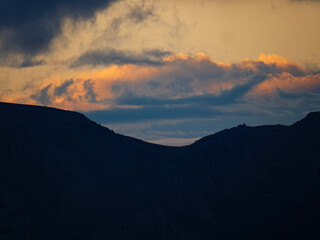Obraz premium A stunning landscape of a mountain silhouette under a heavy dark storm cloud with a beautiful band of golden sunset light