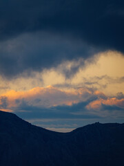 Obraz premium A stunning vertical photograph of a mountain peak silhouette against a dramatic sky with layers of colorful clouds at sunset