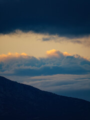 Obraz premium A stunning vertical composition of a mountain silhouette with beautiful golden and blue clouds layered in the sky at sunset