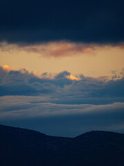 A minimalist vertical photograph of a mountain silhouette with stunning layers of colorful clouds above during a beautiful sunset