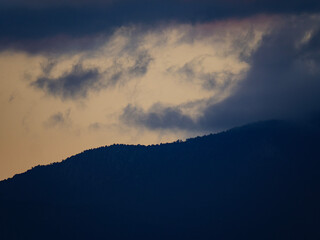 A beautiful abstract of a dark mountain silhouette with a soft moody cloud formation above illuminated by a sunset