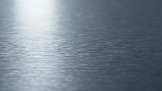Extreme macro close-up of a brushed metal surface with fine parallel lines, gently reflecting ambient light as the camera glides metal, steel, brushed