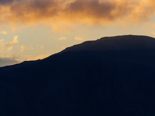 A simple and powerful minimalist landscape of a dark mountain silhouette with beautiful golden sunset light on the horizon