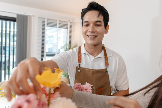 A young couple arranging colorful flowers together in a cozy home setting. The man, wearing an apron, helps the woman create a beautiful bouquet, sharing smiles and creativity in harmony.