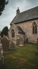 Fototapeta premium Ancient weathered gravestones clustered densely around the exterior walls of a historic stone church building on a cloudy afternoon ,serene ,old ,silence