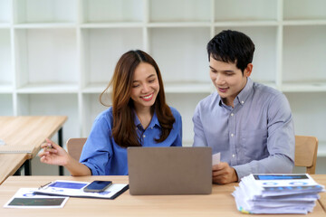 Obraz premium Asian business colleagues collaborating on a project, using a laptop and discussing documents in a modern office environment