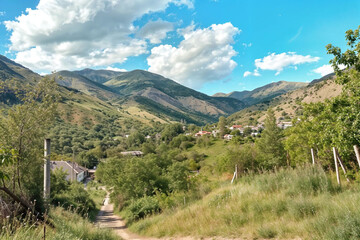 Fototapeta premium Scenic landscape view of valley with mountains and small village. Green hills and summer sky showing peaceful rural nature environment.