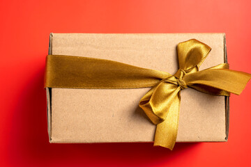 Top view of a brown gift box tied with a golden ribbon on a colored background. Mockup or copy space. Concept of decoration for holidays, anniversaries, celebrations, presents, or surprises