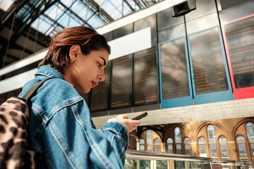 Young woman checking train schedule on smartphone in busy station