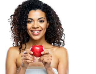 Smiling woman with curly hair holds a red apple against a black background with her shoulders exposed