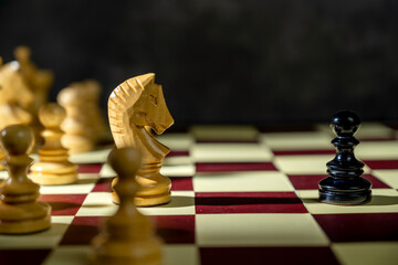 Closeup view of a white chess knight standing against the opposing pieces on the chessboard. Concept of strategy © Leo Lintang
