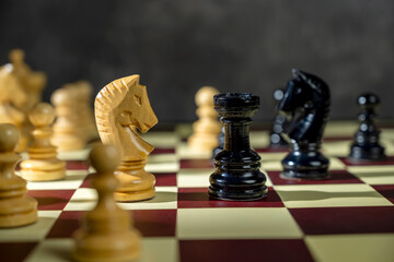 Closeup view of a white chess knight standing against the opposing pieces on the chessboard. Concept of strategy © Leo Lintang