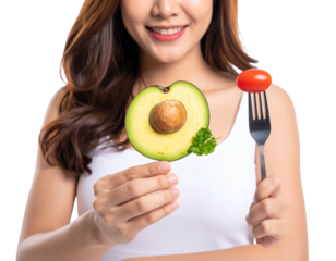 Smiling woman holds avocado half and tomato on fork, against dark backdrop. Healthy eating concept