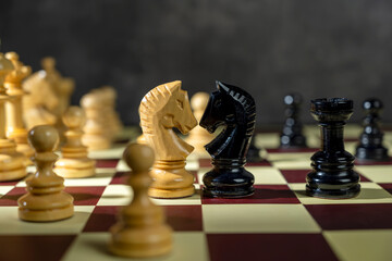 Closeup view of a white chess knight standing against the opposing pieces on the chessboard. Concept of strategy © Leo Lintang