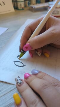 Artistic lettering process with ink pen, focused on handwriting skills. Hand of an artist writing decorative script on paper, demonstrating calligraphy practice and artistic expression.