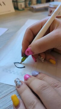 Calligraphy artist working with ink pen, forming graceful letters on paper. Focus on handwriting technique, creative process, and fine art expression.