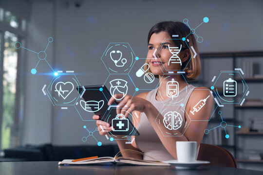Smiling businesswoman in casual wear holding tablet device touching it at office workplace. Concept of distant work, business education, information technology. Health care icons hologram