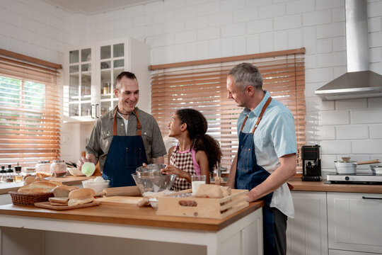 Caucasian senior gay couple baking bakery with adopted daughter in house. 