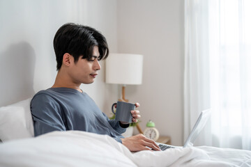 Asian man freelancer drink coffee and using laptop device working in house.