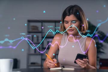 Smiling businesswoman in casual wear holding using smartphone typing at office workplace with notebook. Concept of distant work, business education. Forex graph and charts theme icons hologram
