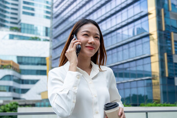 Asian young businesswoman talking on smartphone while standing in city. 