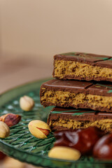 A bar of Dubai chocolate with dates, kadayif and pistachio paste with pistachios, on a green glass surface