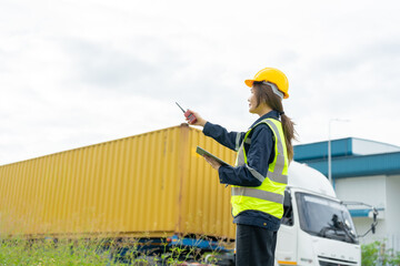 A female engineer wearing a yellow helmet and a tablet stands on a truck-transport road, overseeing mechanical systems, analyzing safety data and ensuring continuous production efficiency at a port.