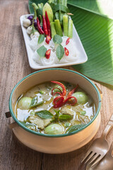 Authentic Thai green curry with tender chicken and eggplants served with rice noodles and fresh vegetables. Traditional Thai food still life on wooden table, beautifully arranged with basil leaves