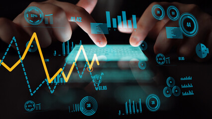 Close-up of hands on a touchscreen device displaying dynamic data analytics and financial trends, emphasizing the integration of technology in business decision-making. Xenic