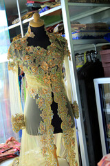 Transparent kebaya dress with brocade and beaded ornaments displayed on a mannequin.