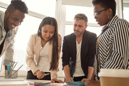 Multiethnic team of young managers working on new project in conference room, standing around table and brainstorming, low angle view