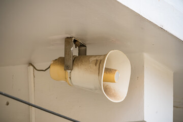 Old dirty white loudspeaker mounted on a ceiling corner of a building used for public announcements...