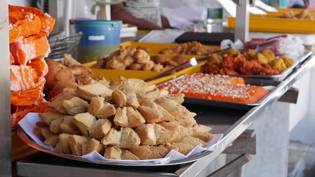Rows of colorful Indian sweets such as jalebi gulab jamun and ladoo displayed on metal trays at a bustling outdoor market. Indian sweets.
