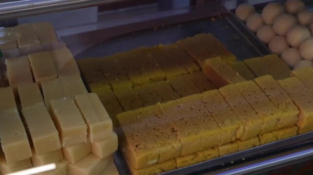 Glass display filled with Indian desserts including jalebi barfi and rasgulla glowing under warm light inside a traditional sweet shop. Indian desserts.