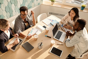 High angle view of young creative office workers of different nationalities sitting at table in conference room and brainstorming