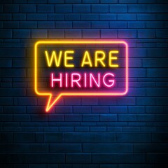 Obraz premium Bright neon 'We Are Hiring' sign illuminates a dark brick wall, signaling exciting career opportunities for ambitious professionals seeking growth and new roles.