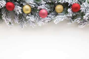Colorful baubles with glitter and green artificial fir branches covered with hoarfrost and white snow. Light gray table background. Closeup. Christmas decoration. Empty place for text. Top down view.