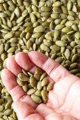 Hand holding green pumpkin seeds over background