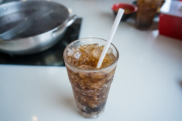 Close-up of a glass filled with iced cola and a straw on a white tabletop in a restaurant setting