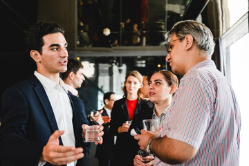 Professionals networking at a corporate event, engaged in conversation and holding drinks in a modern venue.