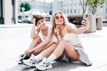Two young beautiful smiling hipster female in trendy summer white t-shirt and shorts clothes. Sexy...