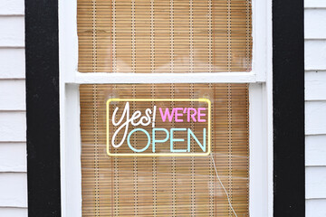 Neon "Yes! We're Open" sign on bamboo-covered window