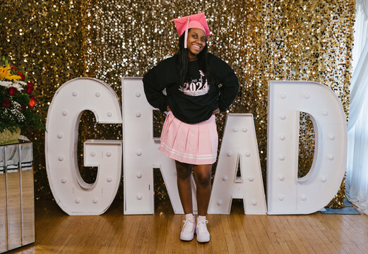 Black teenage girl in graduation sweatshirt and pink cap