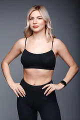 Fototapete Gymnastik Beautiful young blonde woman in black sportswear on a gray background  © Cavan